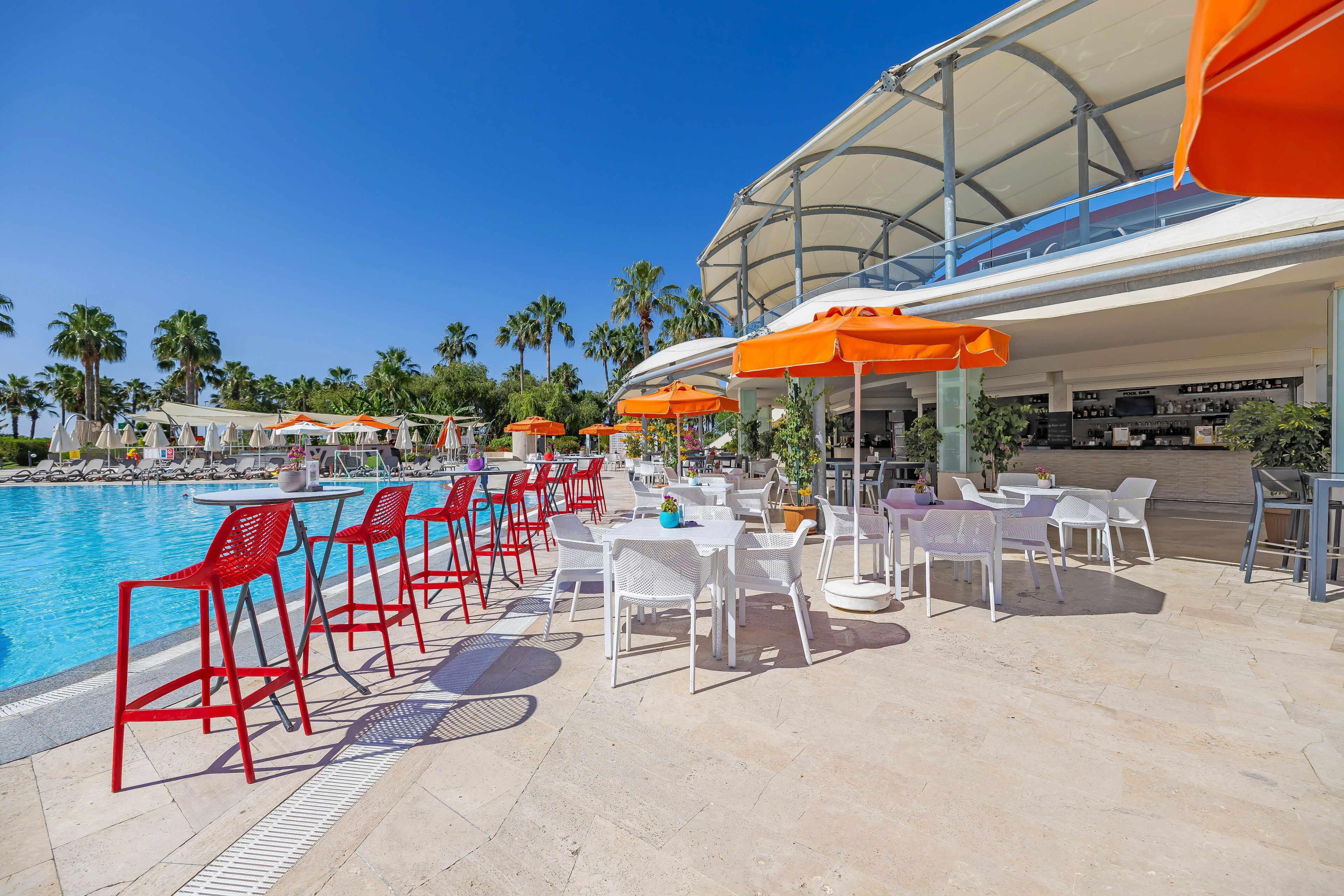 A poolside area with red and white chairs, orange umbrellas, and a bar area.