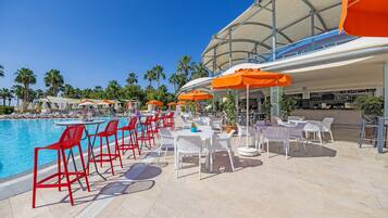 A poolside area with red and white chairs, orange umbrellas, and a bar area.