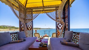 Un espace aménagé avec des sièges, situé au bord de la plage, avec une table dressée pour deux personnes, offrant une vue sur la mer.