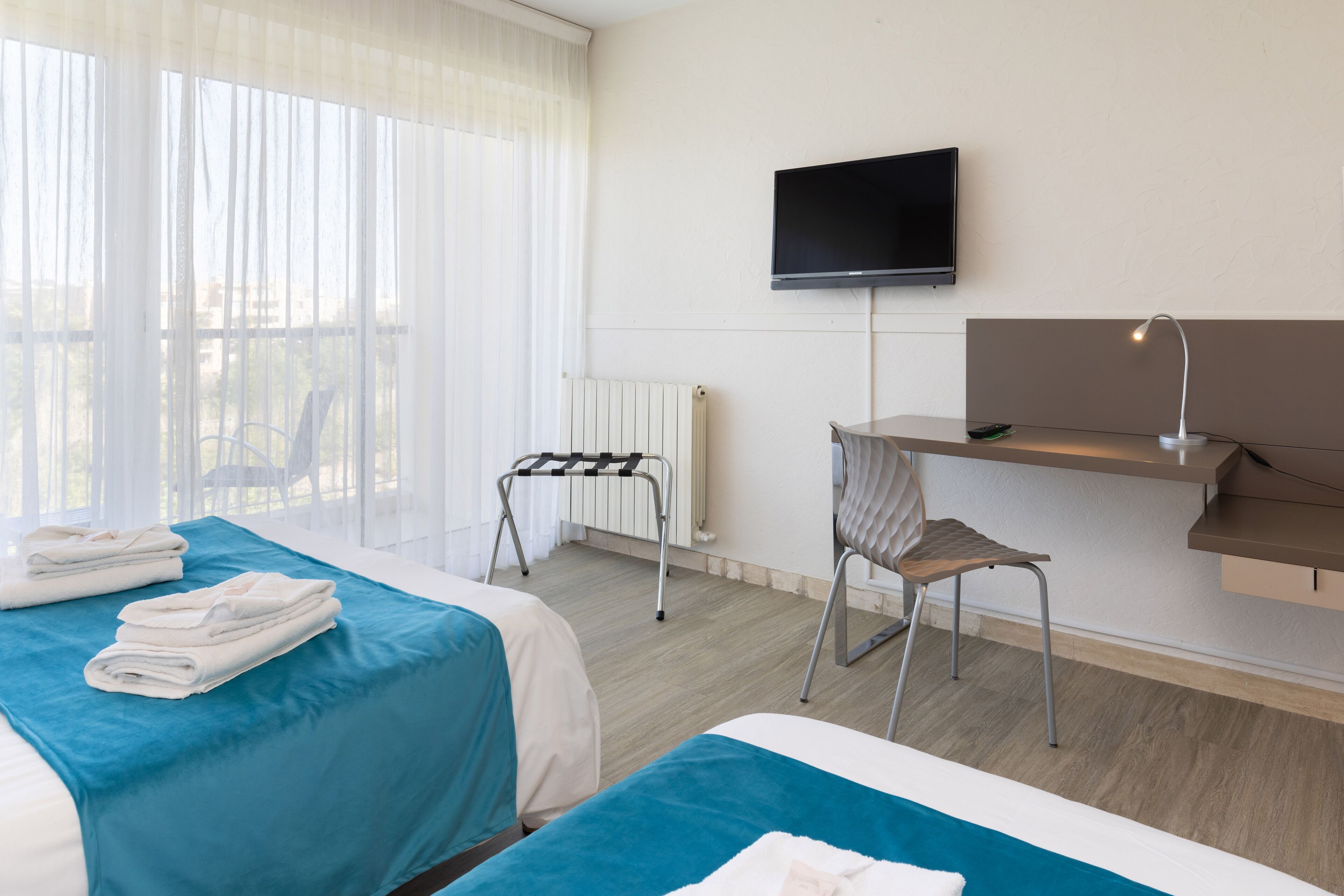 Une chambre d’hôtel avec deux lits, une télévision, un bureau avec une lampe et une chaise.