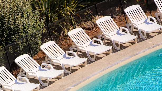 Piscina com cadeiras de descanso brancas e uma pessoa nadando.