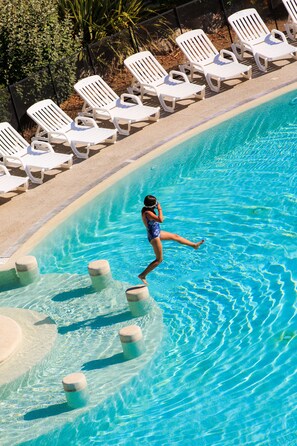 A swimming pool with white lounge chairs and a person swimming. - Hotel Club Le Capet (Sainte-Maxime)