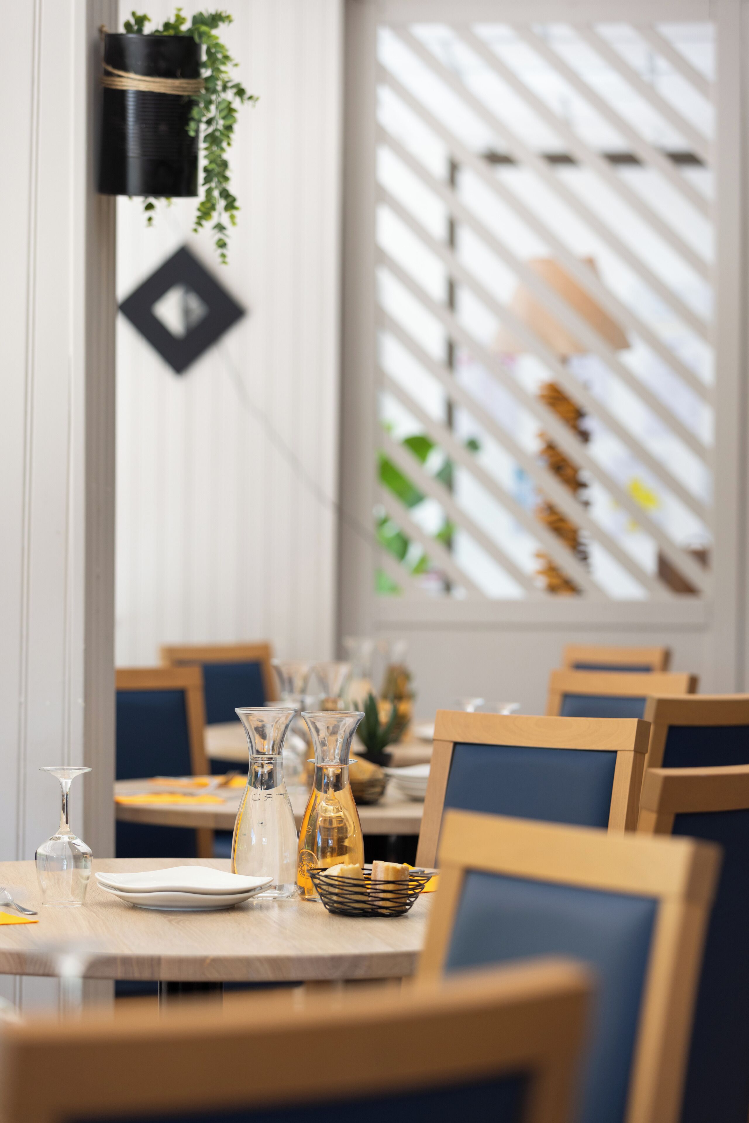 Un coin repas avec une table dressée pour deux personnes, agrémenté d’un vase, d’une carafe en verre et d’un panier de pain.
