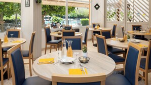 Restaurante com mesas redondas, cadeiras azuis e guardanapos amarelos.