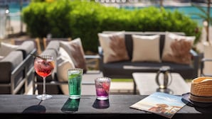 Uma área de bar com bebidas e um cardápio, mesas ao ar livre e uma piscina ao fundo.