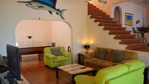 A living room with a television, two sofas, a coffee table, and a staircase. - Casa Rosa (Cabo San Lucas)