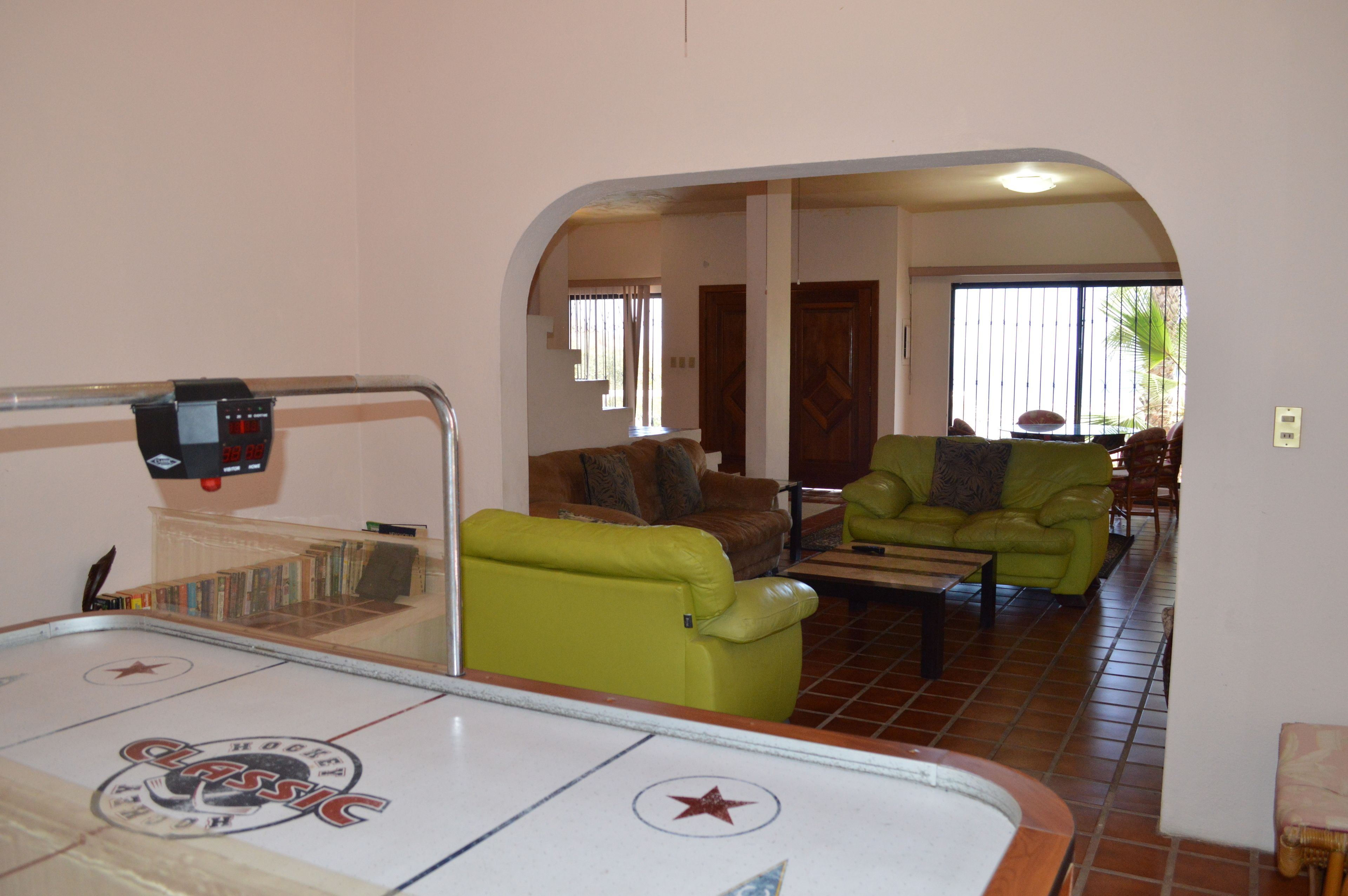 A room with a pool table, green sofas, and a dining area.