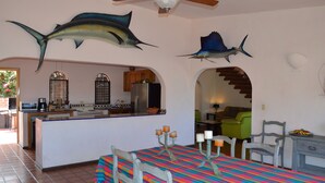 A dining area with a colorful tablecloth, a ceiling fan, and decorative fish mounted on the wall. - Casa Rosa (Cabo San Lucas)
