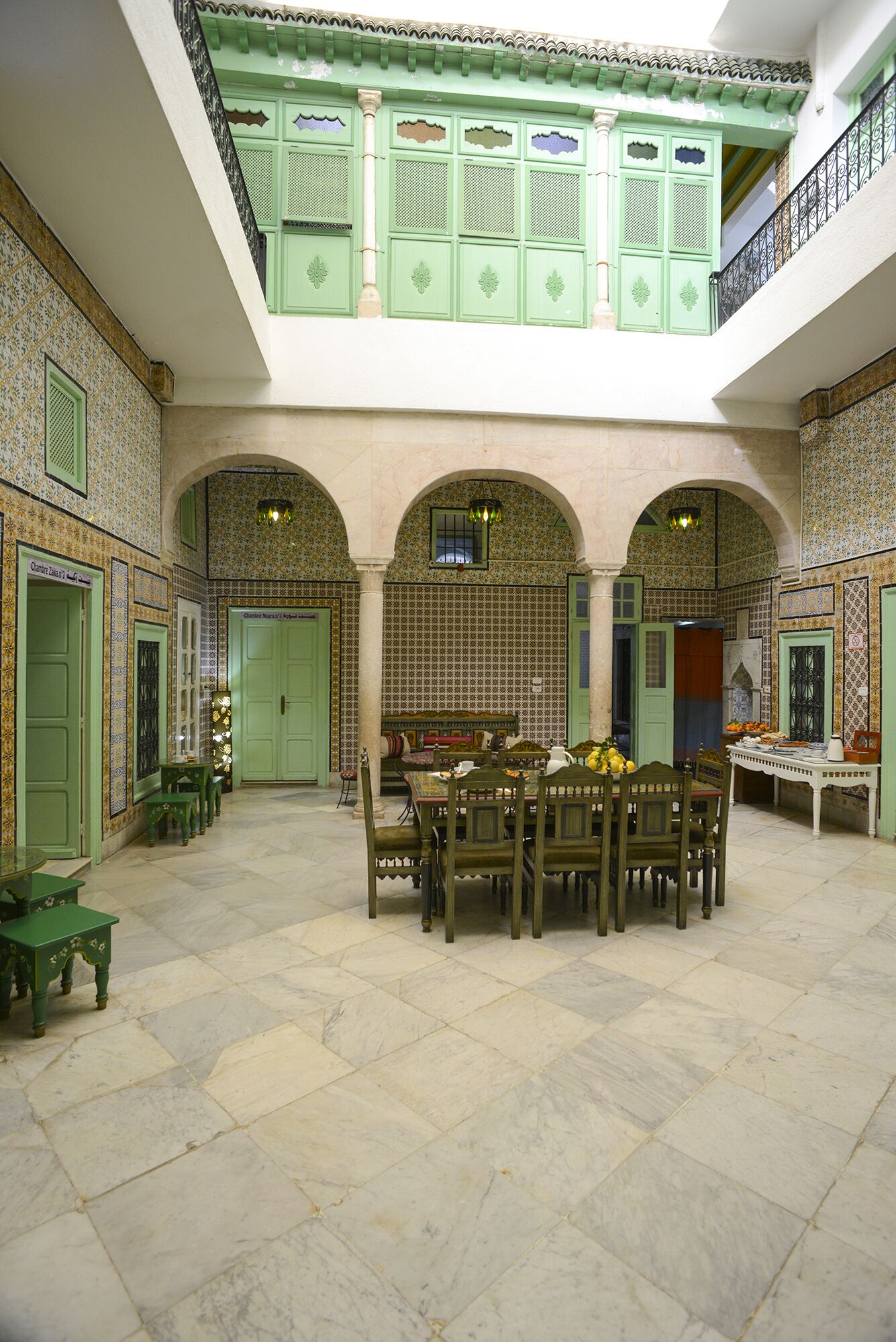 A spacious courtyard with a central dining area, green doors, and tiled walls.