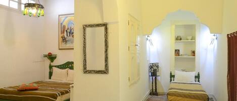 A spacious room with a large arched doorway, a dining area with a table and chairs, and a bed with a striped bedspread.