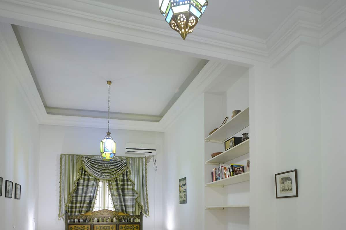 A bedroom with a bed, bedside tables, a desk, a chair, a colorful striped rug, a hanging light fixture, and a bookshelf.