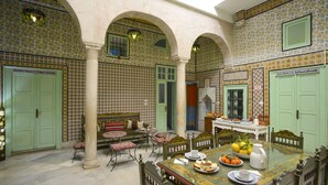 A traditional Moroccan interior with a dining area featuring a table set with plates, a pitcher, and a bowl of fruit. There are green doors and patterned tiles on the walls. - Dar Ya - Hostel (Tunis)
