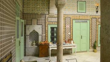 Un interior tradicional marroquí con azulejos estampados, una puerta verde y un patio con asientos y mesas.
