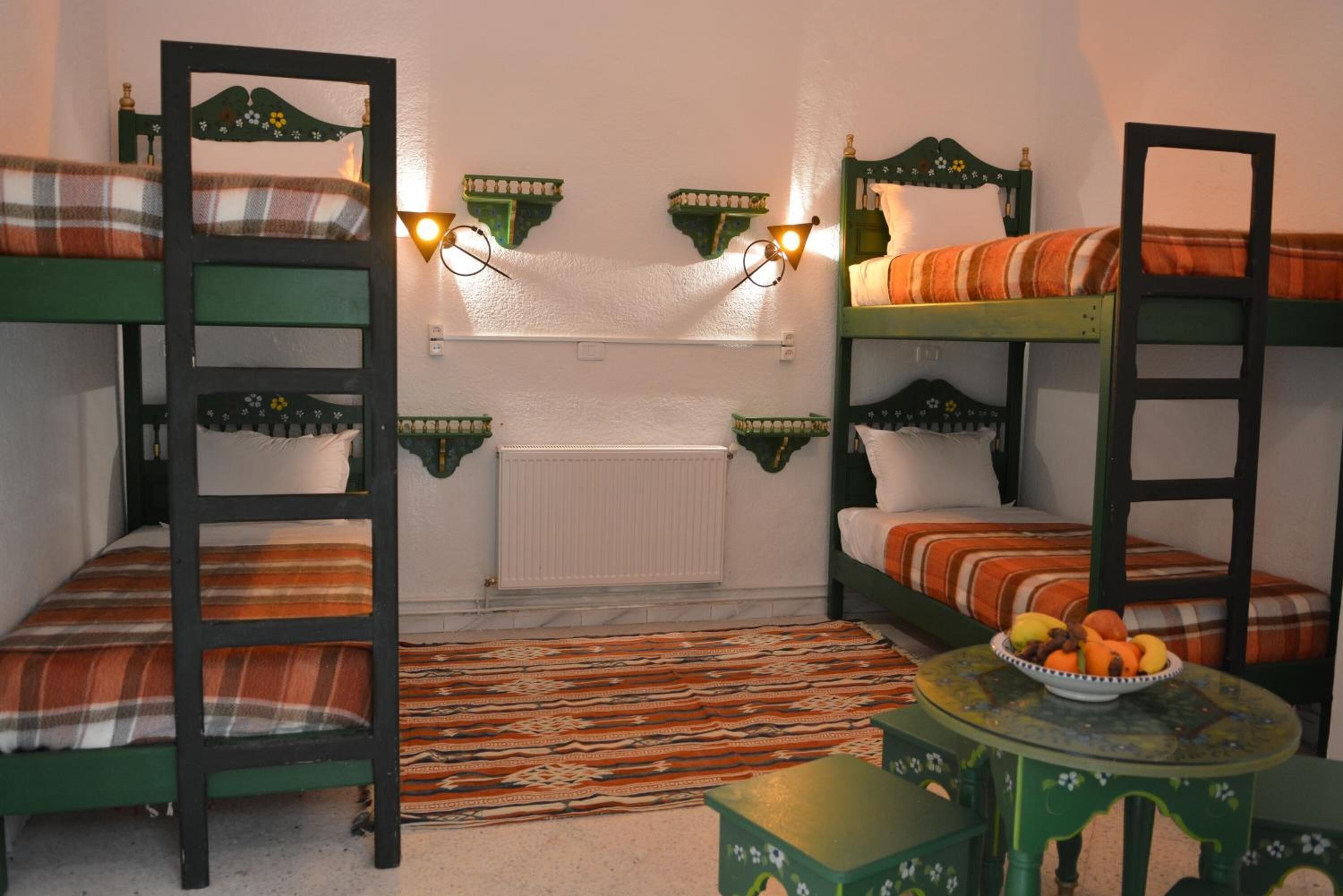 A room with bunk beds, a radiator, a patterned rug, and a small table with a fruit bowl.