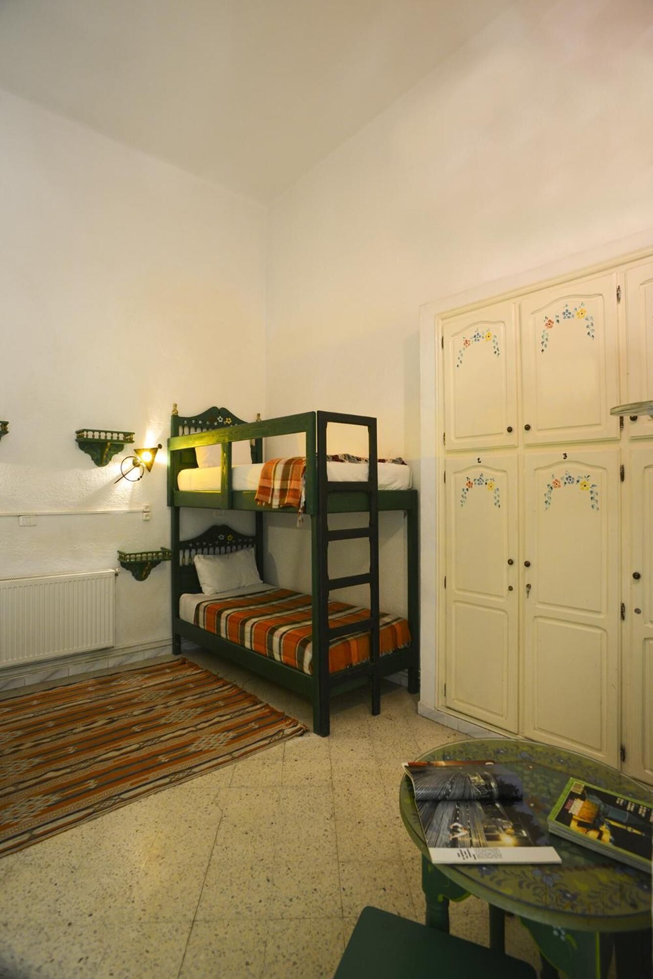 A bunk bed room with a radiator, a small table, and a cabinet.