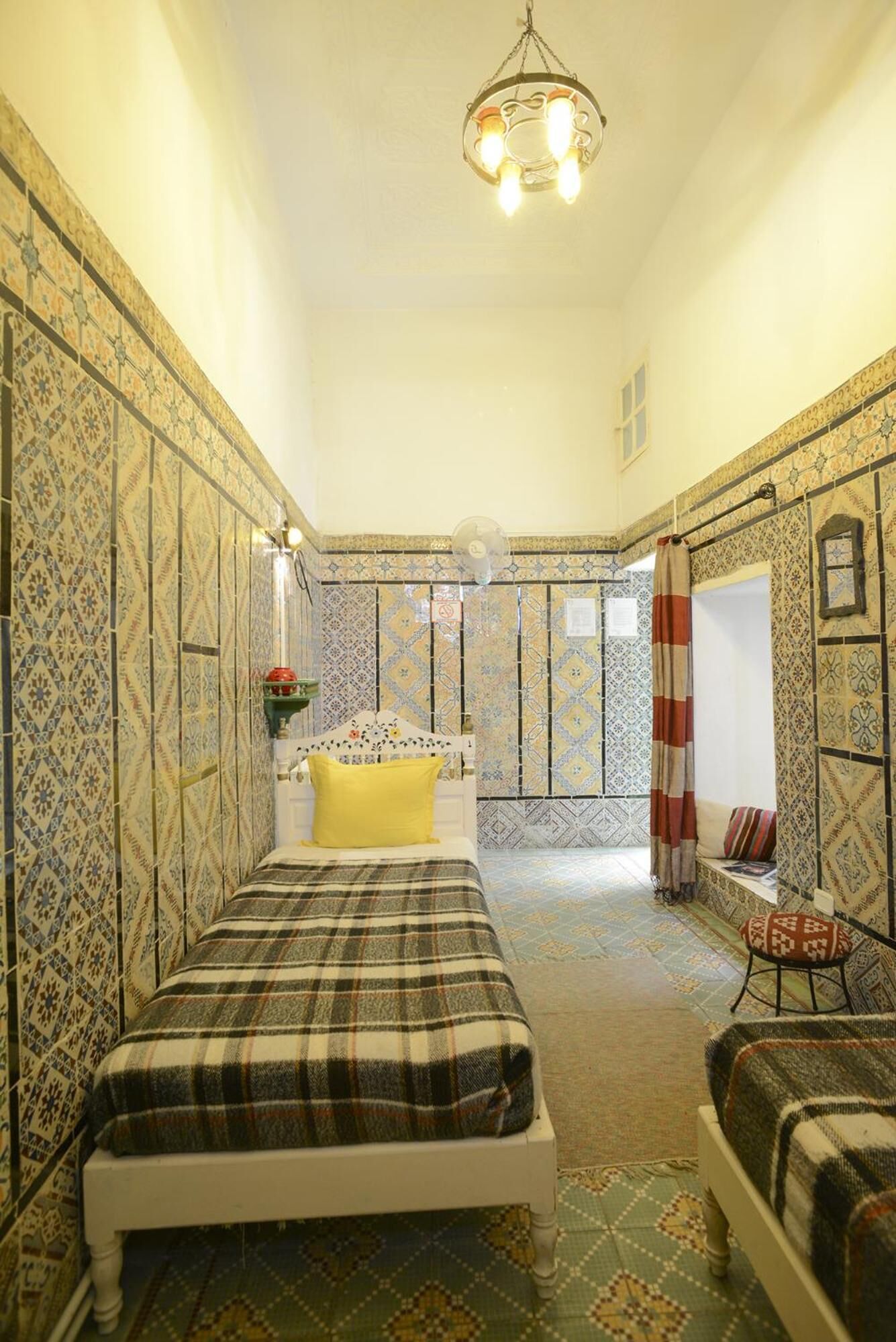 A room with a bed, a chair, a small table, a mirror, and a hanging light fixture.