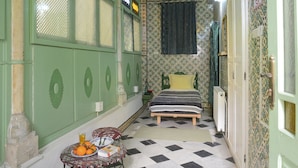 A room with a checkered floor, a bed with a striped blanket, a table with oranges and a book, and a fan on the ceiling. - Dar Ya - Hostel (Tunis)