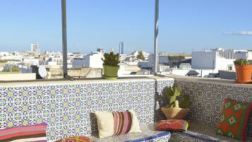 Une terrasse sur le toit, agrémentée d’un mur décoré de motifs, d’un espace salon et d’une table où sont disposés des fruits et des boissons.