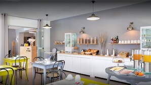 Un área de desayuno de hotel moderna con mesas amarillas y grises, una vitrina de vidrio y un mostrador de buffet con diversas opciones de comida.
