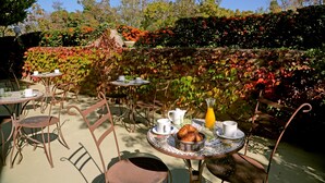 Un café al aire libre con mesas y sillas, rodeado de follaje y árboles exuberantes.
