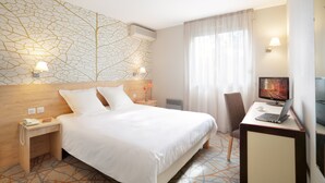 Habitación de hotel con cama, escritorio con computadora portátil, televisor, teléfono y un diseño de árbol en la pared.