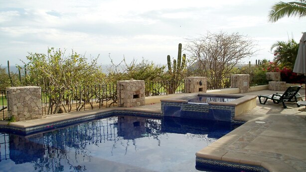 Una piscina con pilares de piedra y un muro de piedra, rodeada de árboles y una valla.