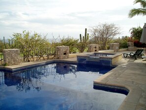 A swimming pool with stone pillars and a stone wall, surrounded by trees and a fence. - Cabo Vista (Cabo San Lucas)