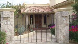 Una entrada protegida por un muro de piedra, techo de tejas y un pequeño porche con un banco.