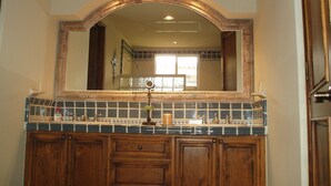Un baño con tocador de madera, salpicadero de azulejos y un espejo grande con arco.