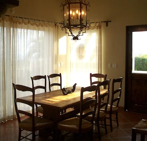 A dining area with a wooden table and six chairs, a chandelier, and a window with curtains.