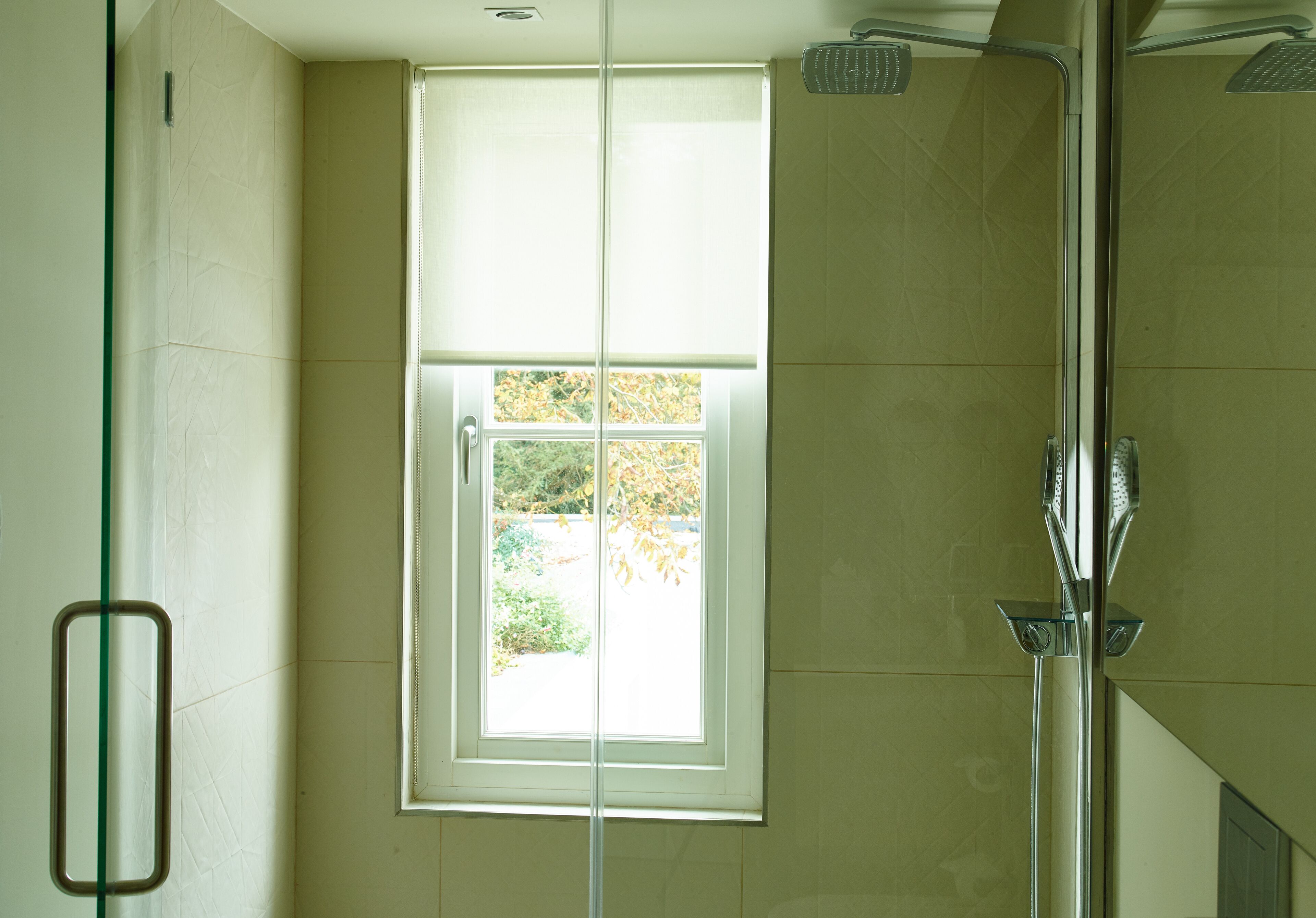 A bathroom with a glass shower enclosure, a window with a view of trees, and a towel rack.