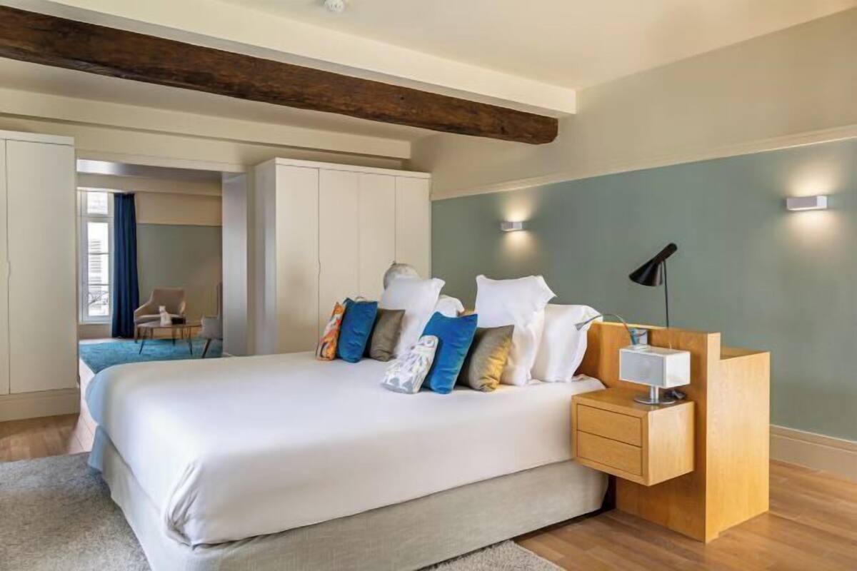 A bedroom with a large bed, bedside tables, a wardrobe, and a view of a blue room.
