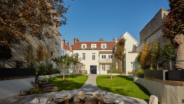 A courtyard with a stone pathway leading to a building, surrounded by greenery and a small pond. - Hôtel de Cavoye (Fontainebleau)