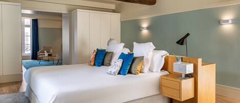 A bedroom with a large bed, a wooden nightstand, and a desk. There is a chair and a wardrobe in the background.