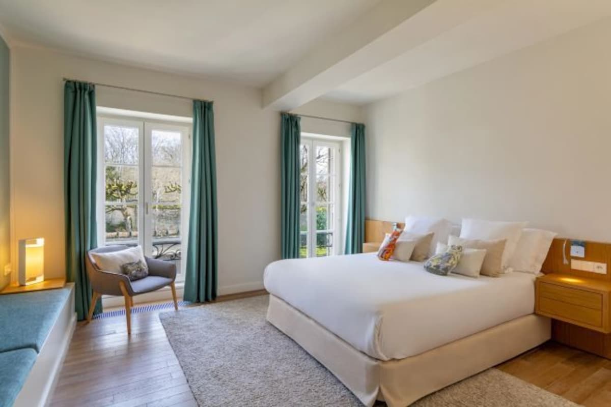A bedroom with a bed, a chair, a nightstand, and a window with curtains.