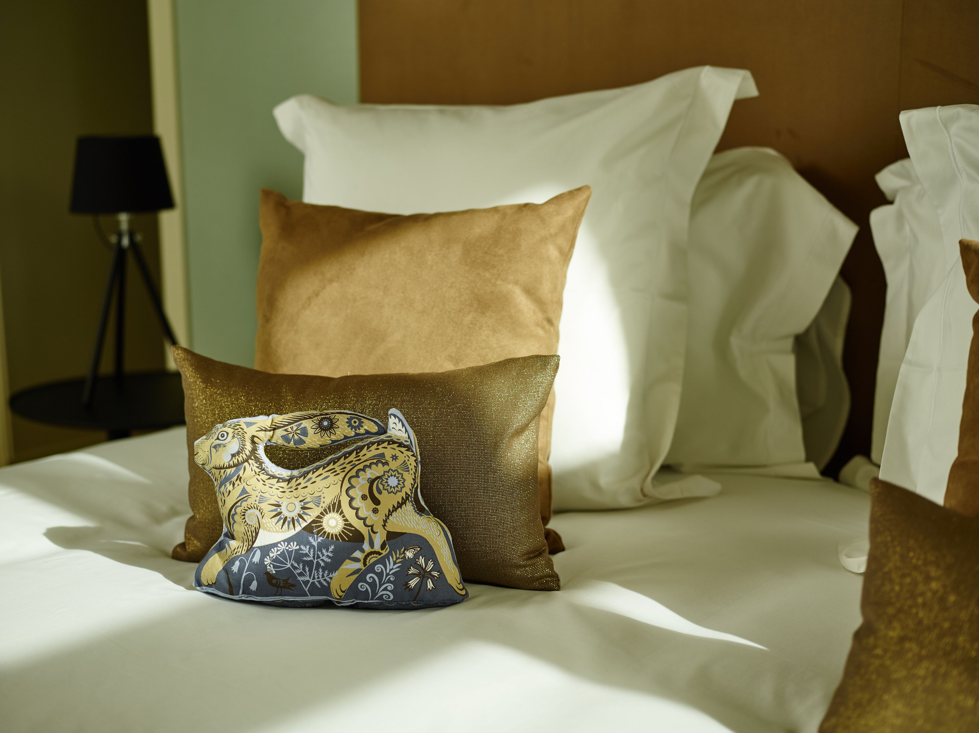 Una cama con un cojín decorativo de diseño dorado y azul, un cojín marrón liso y un cojín blanco.