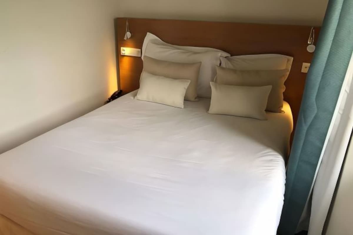 A neatly made bed with a wooden headboard, a bedside lamp, and a window with curtains.
