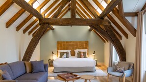 A bedroom with a large bed, a sofa, a chair, and a small table. The room has wooden beams on the ceiling and a window with curtains. - Hôtel de Cavoye (Fontainebleau)