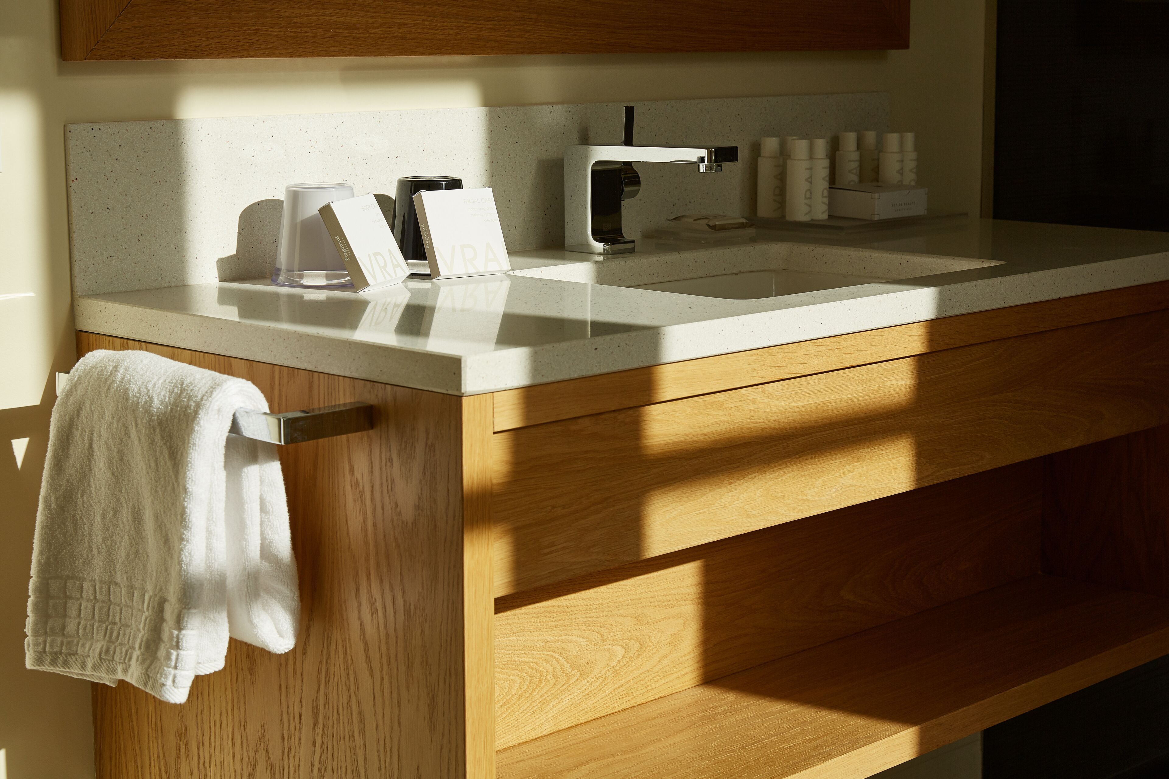 A modern bathroom with a white countertop, wooden cabinetry, a towel rack, and a sink with a faucet.