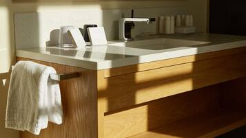 A modern bathroom with a white countertop, wooden cabinetry, a towel rack, and a sink with a faucet.