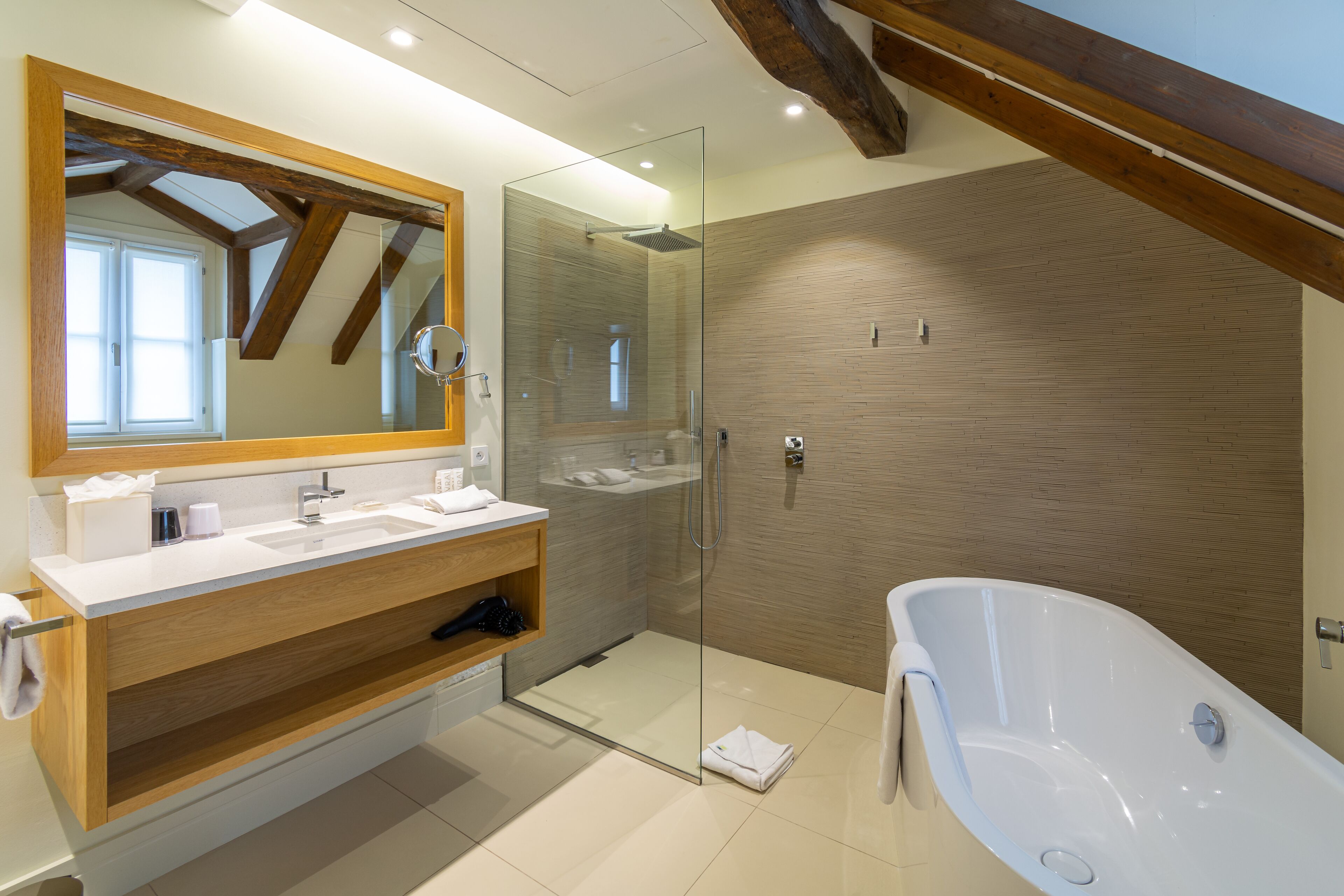 Un baño moderno con un espejo grande, dos lavamanos, una ducha con mampara de vidrio y una bañera independiente.