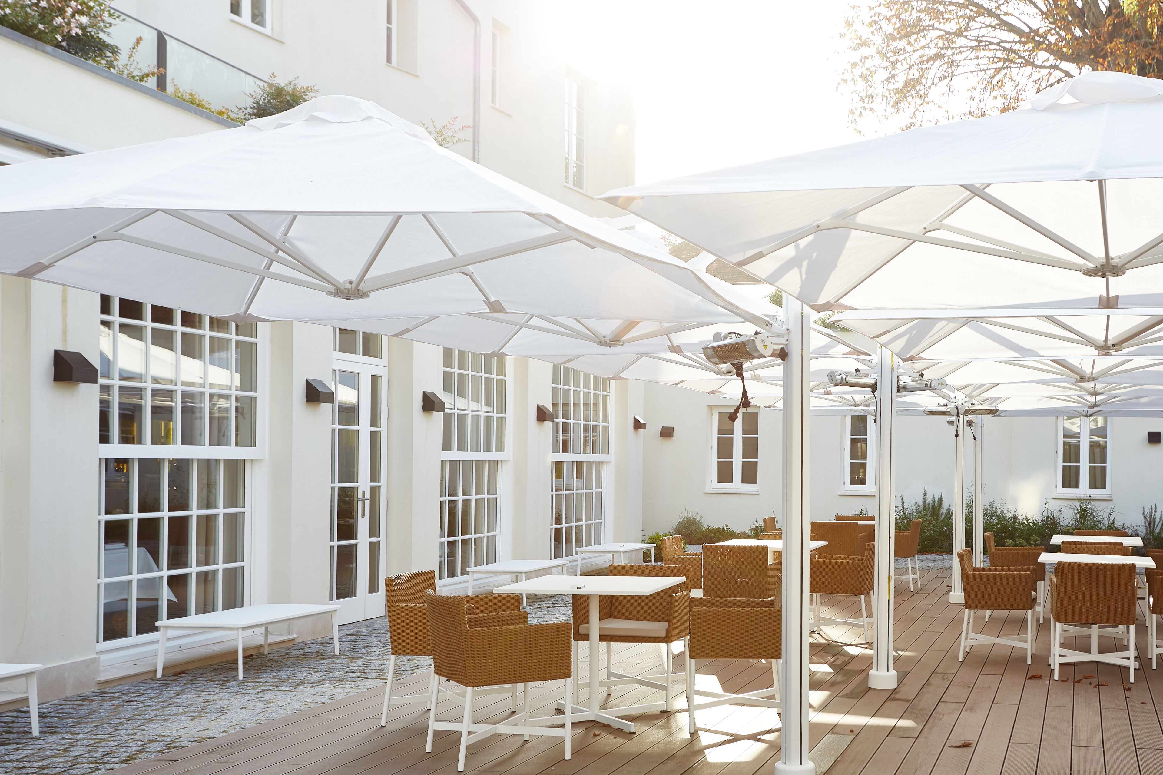 An outdoor patio with white umbrellas, wicker furniture, and large windows.