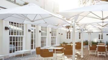 An outdoor patio with white umbrellas, wicker furniture, and large windows.
