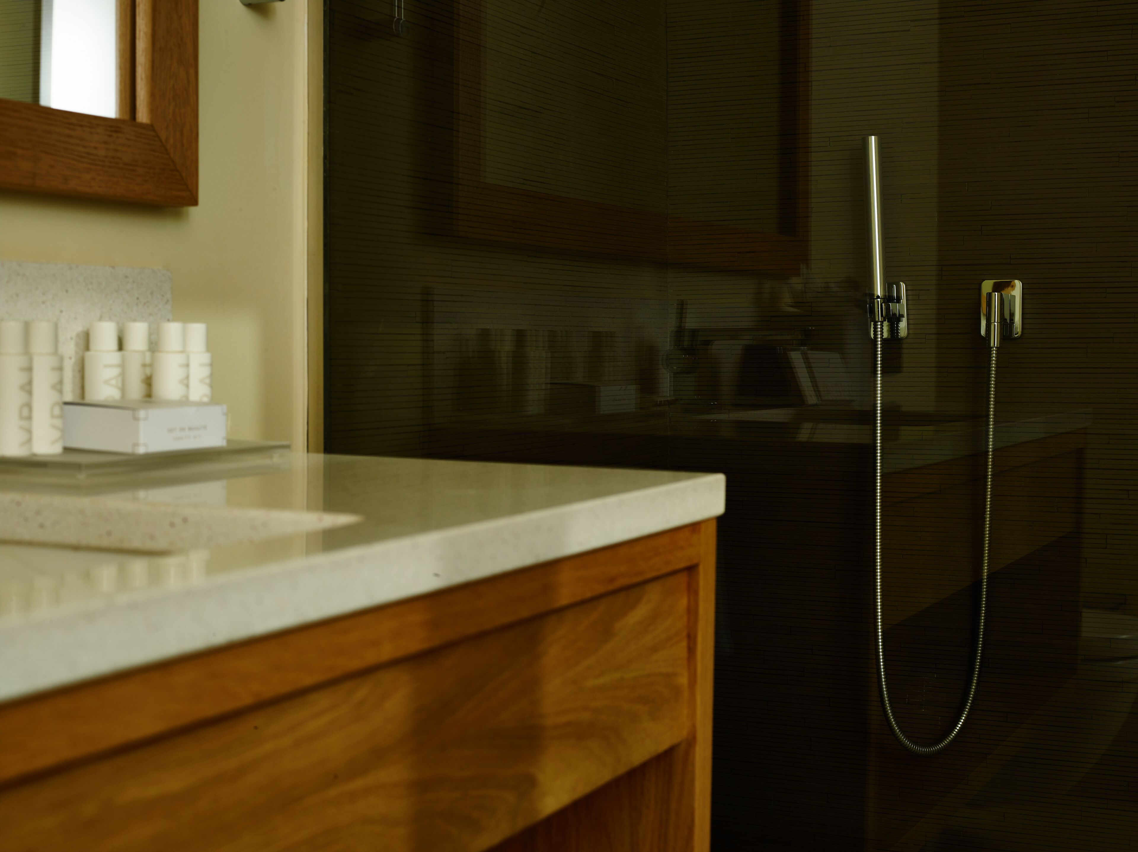 Un baño con tocador de madera, espejo y ducha con cabezal de ducha manual.