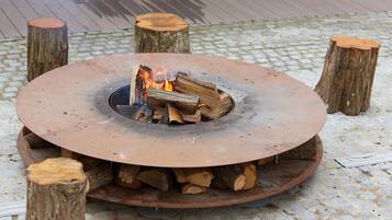 A circular fire pit with logs and flames, surrounded by four wooden stumps, set on a cobblestone surface.
