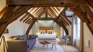 A bedroom with a large bed, a sofa, a small table, and a chair. The room has wooden beams on the ceiling and a window with curtains. - Hôtel de Cavoye (Fontainebleau)