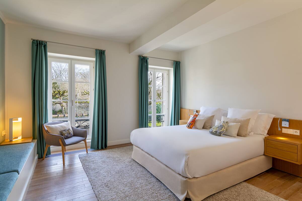A bedroom with a large bed, a chair, a bedside table, and a window with curtains.