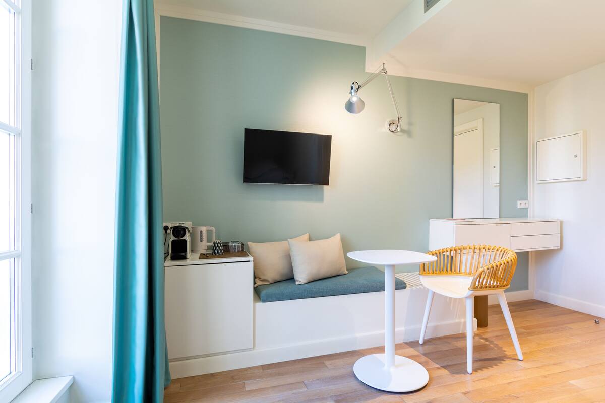 A modern room with a sofa bed, a small table, a chair, a TV mounted on the wall, and a mirror.