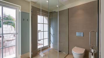 A modern bathroom with a glass shower enclosure, a toilet, and a large window providing natural light.