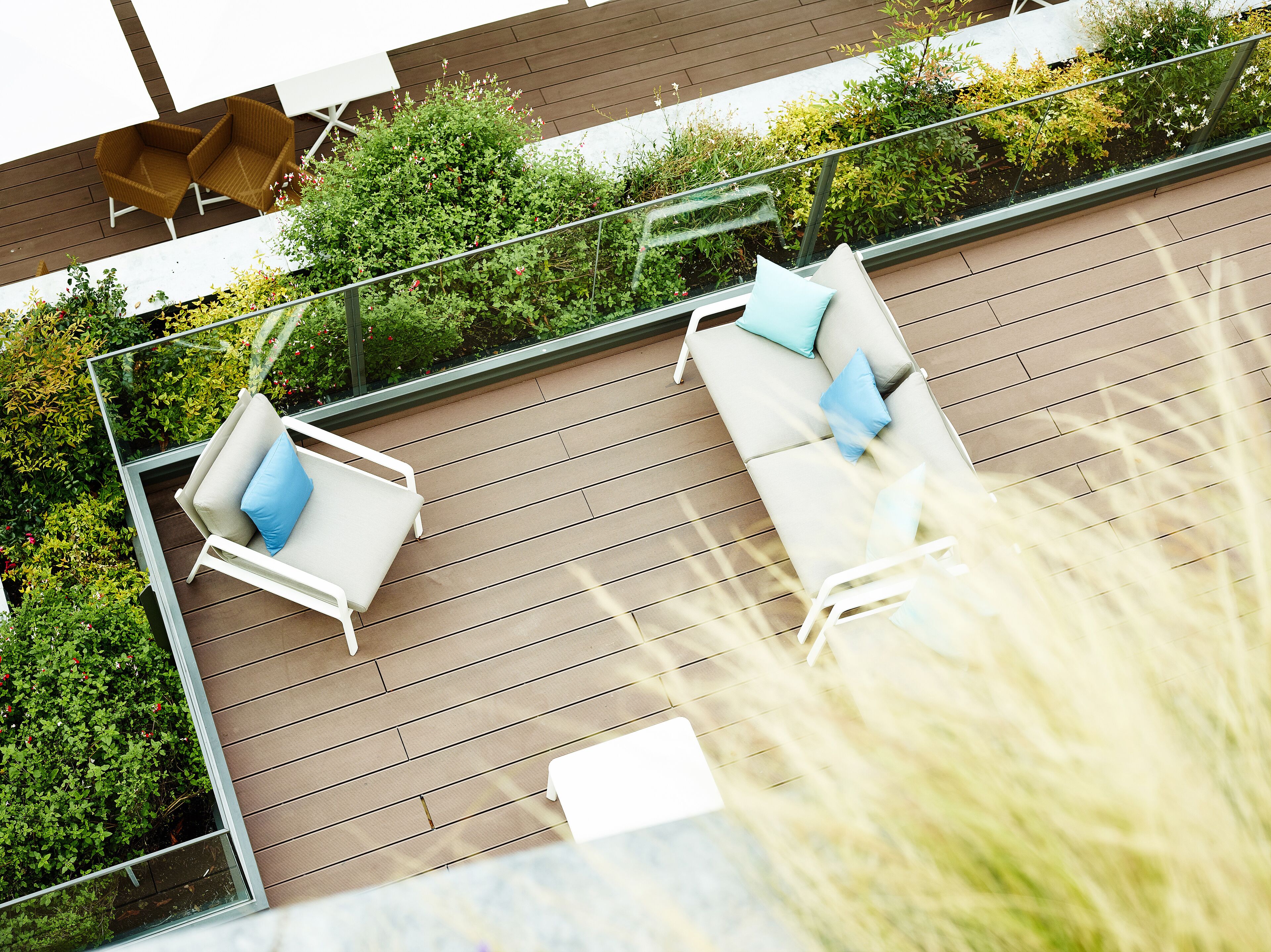 Eine Dachterrasse mit zwei weißen Liegestühlen, einem Glasgeländer und üppiger Bepflanzung.